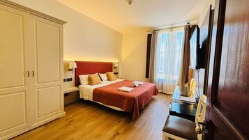 Una habitación de hotel con cama, escritorio, armario y televisor.