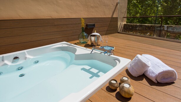 A hot tub with a wooden deck, a bottle of champagne, and a towel. - Hotel Central Maria (Maria de la Salut)