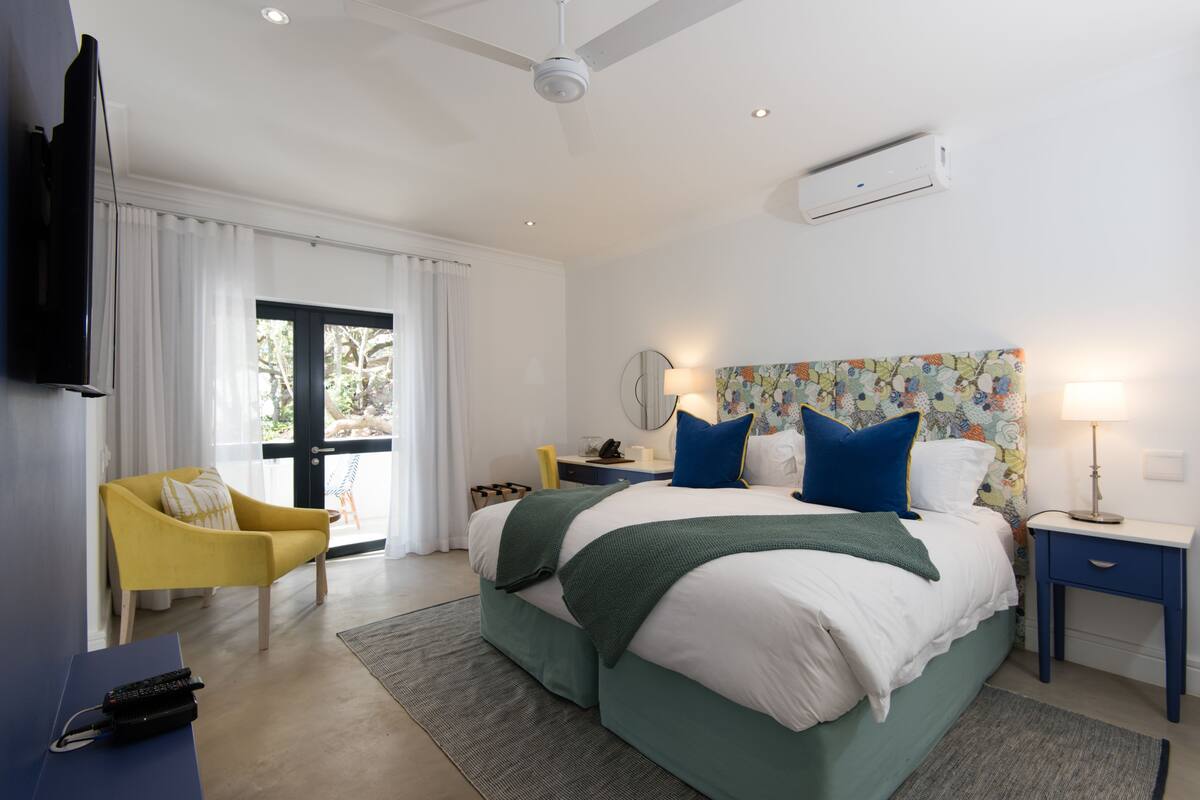 A bedroom with a bed, a chair, a desk, a TV, and a window.