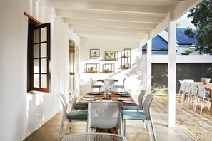 A dining area with a long table, chairs, and a pergola overhead. - The Old Rectory (Plettenberg Bay)