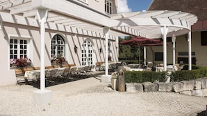 A covered outdoor seating area with tables and chairs, a pergola, and a red umbrella. - Schlossgut Odelzhausen (Odelzhausen)