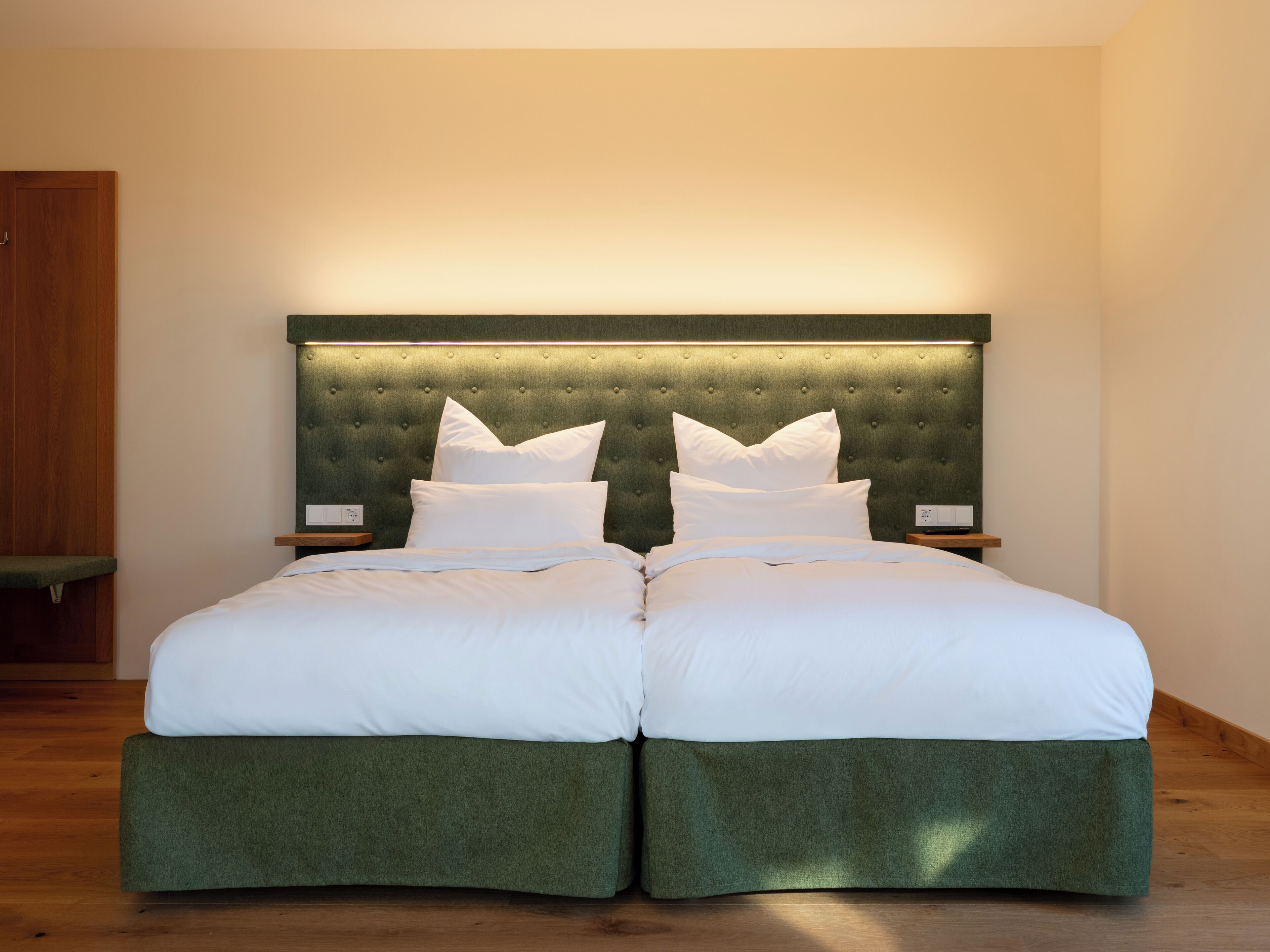 A double bed with a tufted headboard, two bedside tables, and a green upholstered footboard.