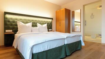 A modern bedroom with a large bed, green upholstered headboard, white bedding, and wooden flooring.