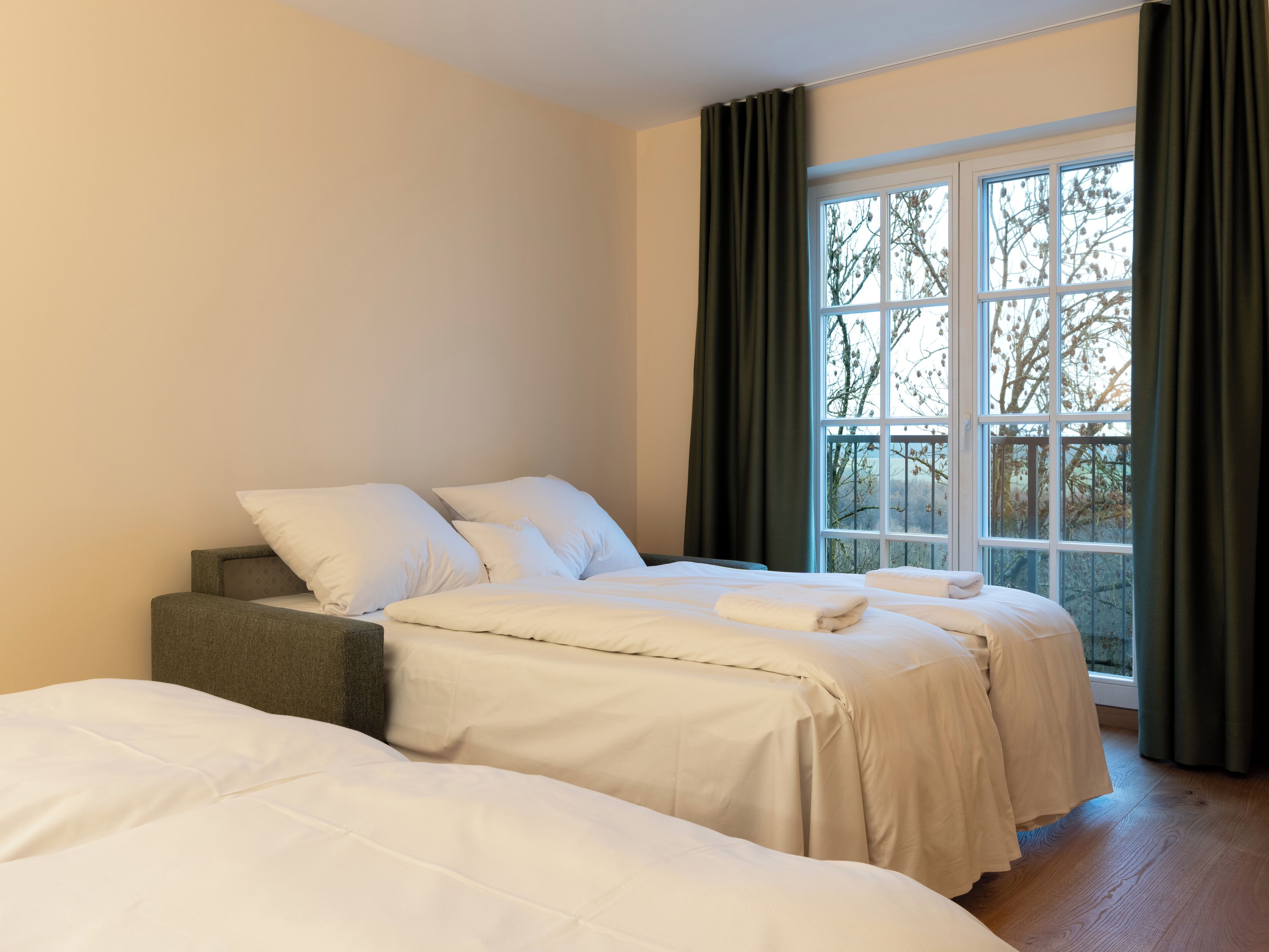 A hotel room with two beds, a window with curtains, and a view of trees.