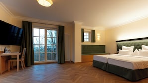 A hotel room with a bed, a desk with a chair, a television, and a large window with curtains. - Schlossgut Odelzhausen (Odelzhausen)