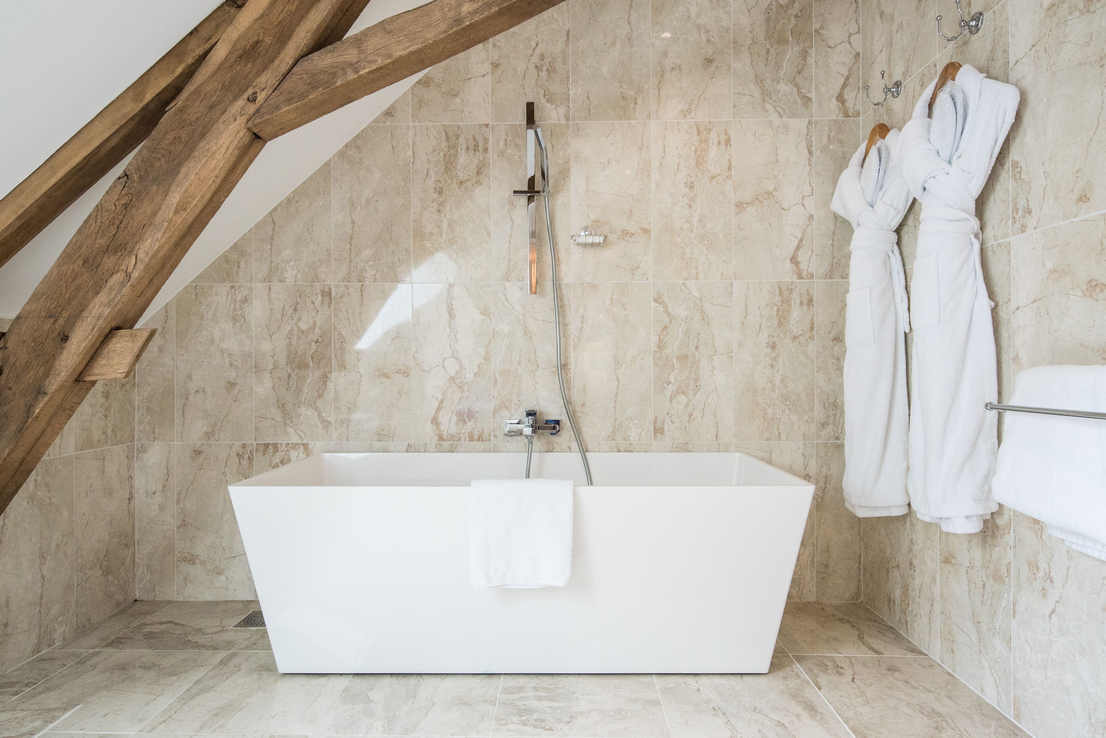 Une salle de bain moderne avec une baignoire sur pieds, des murs en marbre et des poutres en bois.