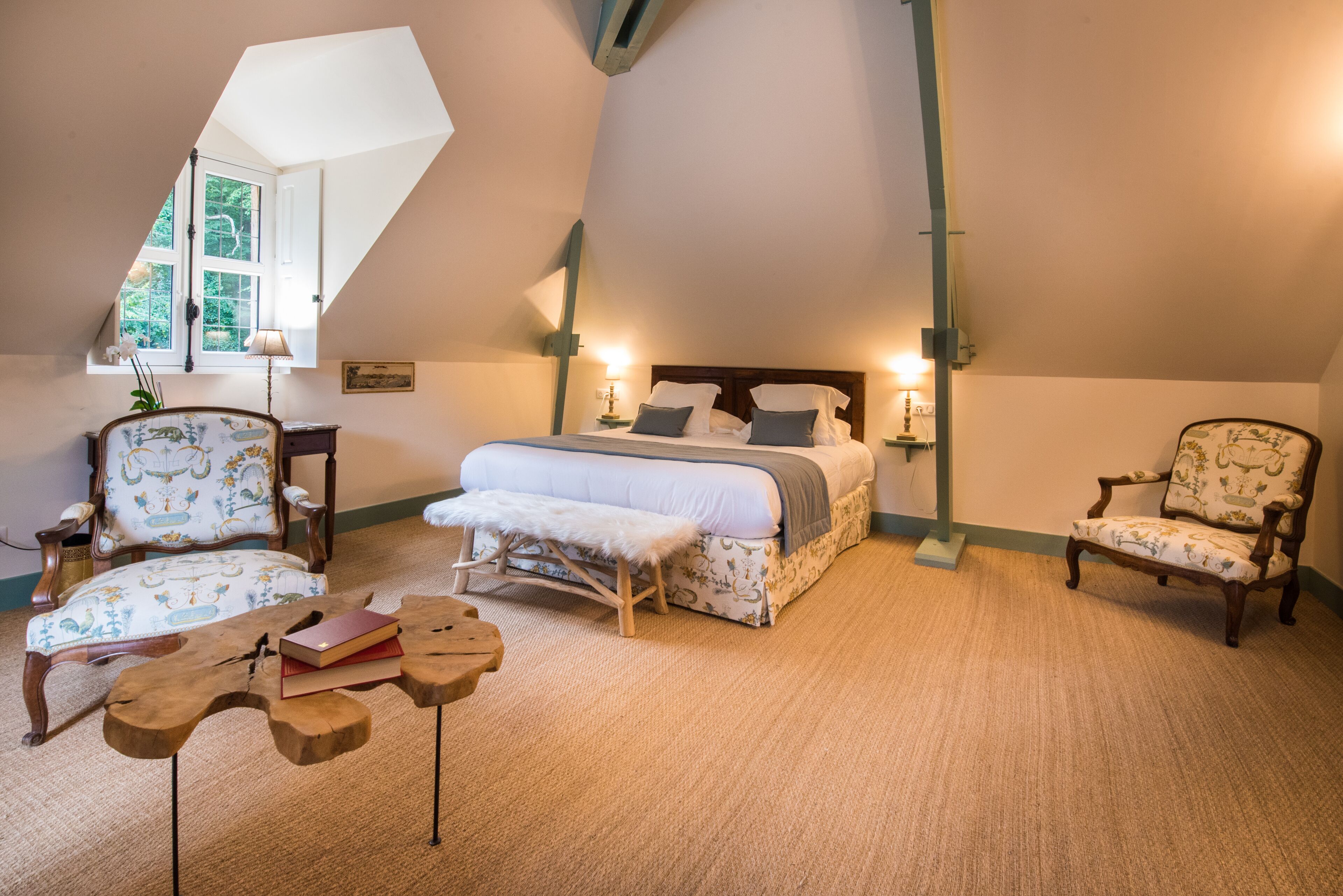 Un dormitorio con cama elevada, dos sillones tapizados, una mesita de centro de madera y una pequeña mesita auxiliar.