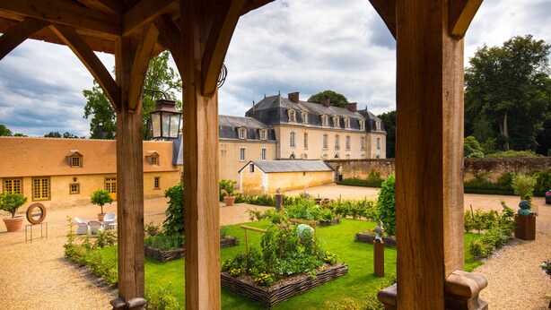 A courtyard with a garden, wooden pergola, and a large building in the background. - Domaine de La Groirie - Le Mans Ouest (Trange)