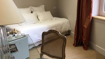 A hotel room with a bed, a desk with a lamp, a chair, and a window with curtains.