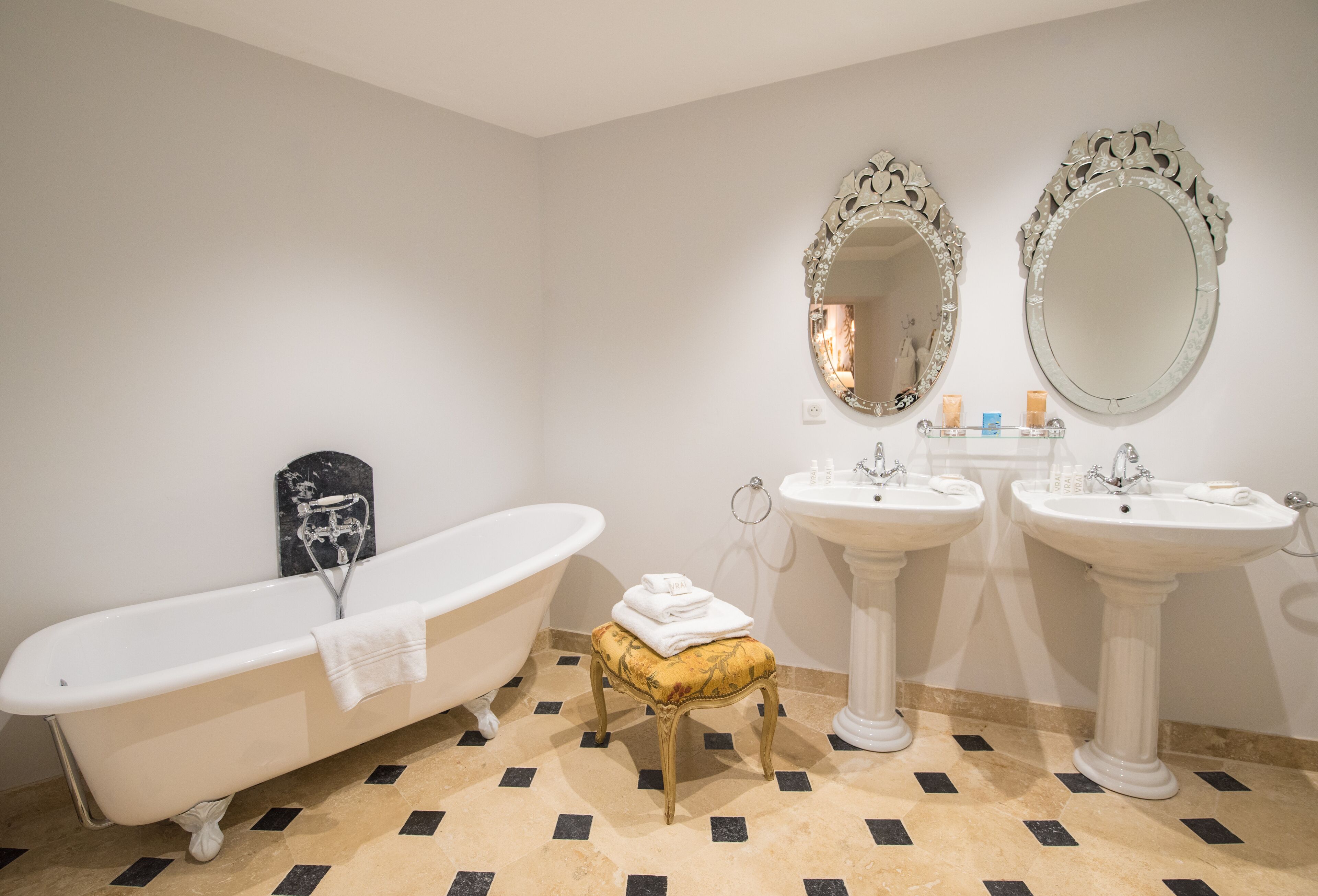 Ein Badezimmer mit einer freistehenden Badewanne, zwei Waschbecken auf Konsolen und zwei Spiegel an der Wand.
