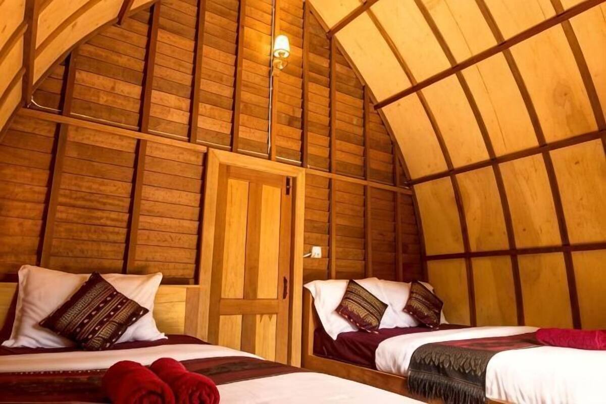Une pièce chaleureuse, aménagée comme un chalet en bois, avec deux lits, une porte en bois et un plafond en pente.