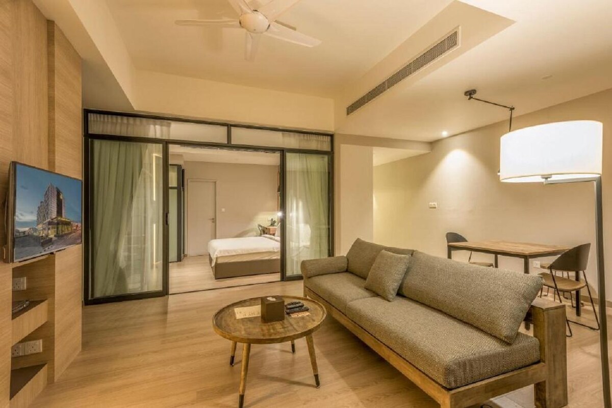 A modern hotel room with a sofa, a small round table, a bed with a sliding door, and a ceiling fan.