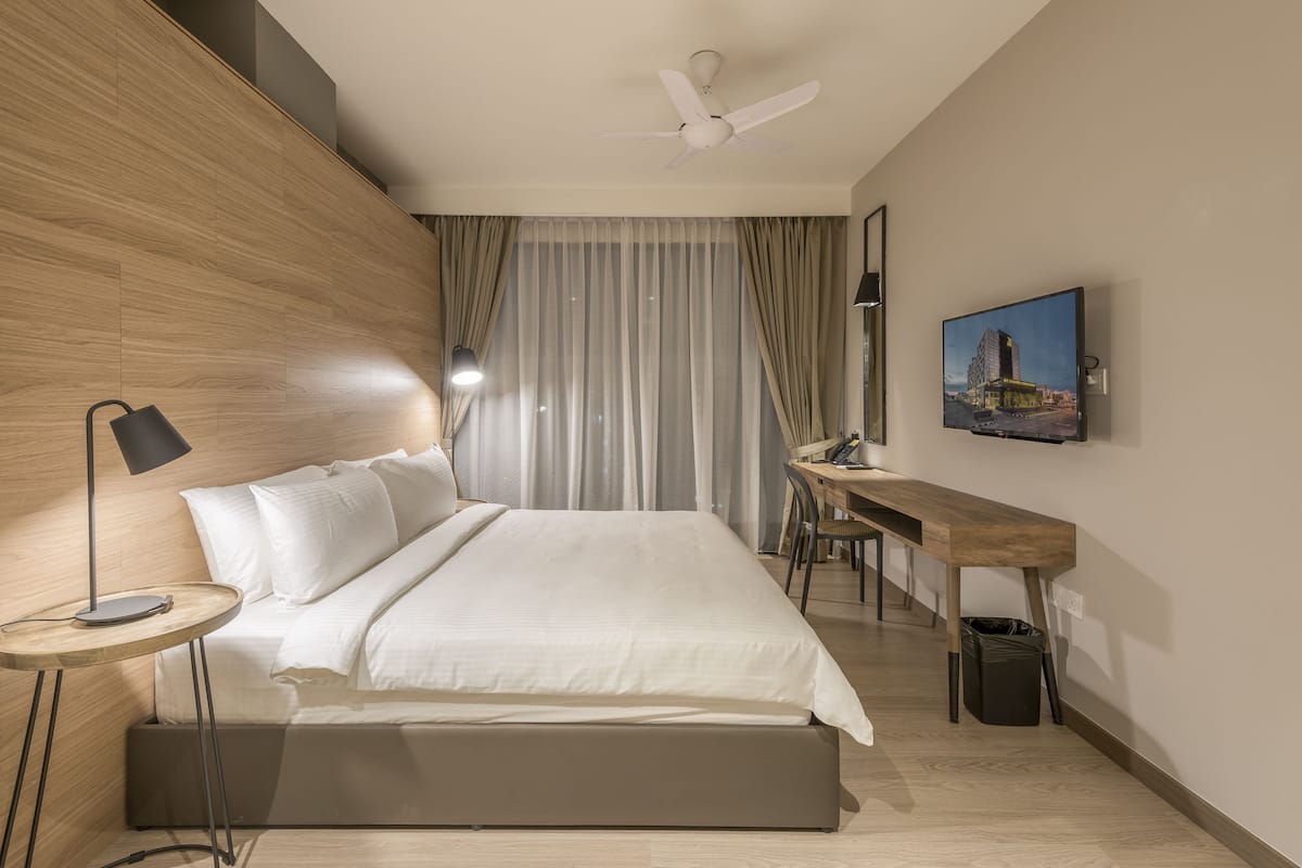 A modern hotel room with a bed, desk, and a large window with curtains.