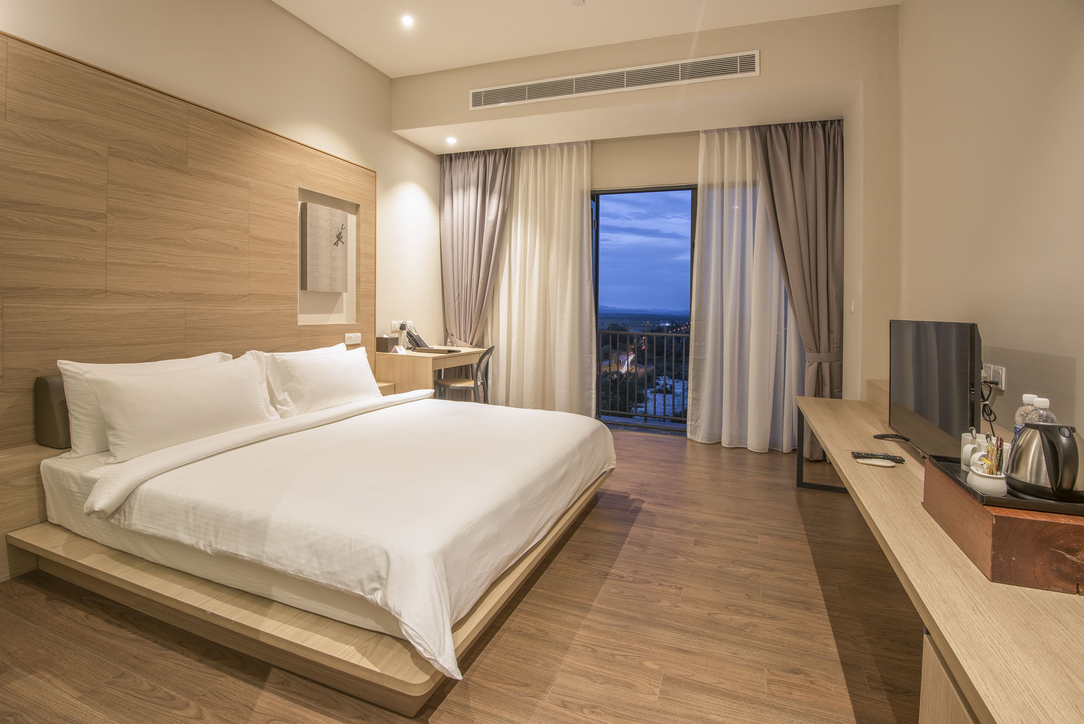 Een moderne hotelkamer met een groot bed, een bureau, een televisie en een balkon met uitzicht op de stad.
