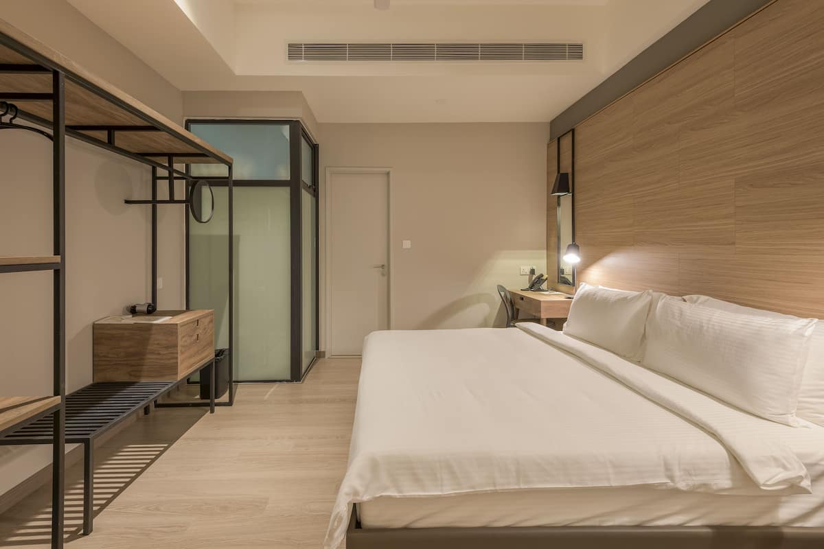 A modern hotel room with a bed, a desk, a chair, a wardrobe, and a shower area.
