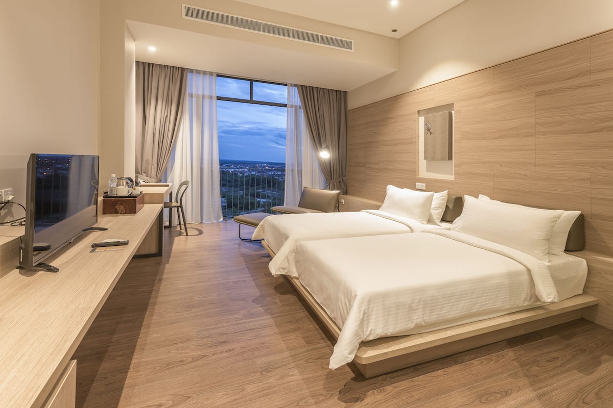 A modern hotel room with a large bed, a desk with a TV, and a view of the city.