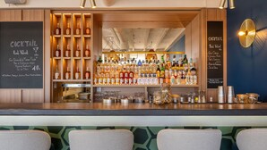 A bar area with a variety of liquor bottles, a chalkboard menu, and bar stools. - Hôtel Café Miramar (Le Grau-Du-Roi)
