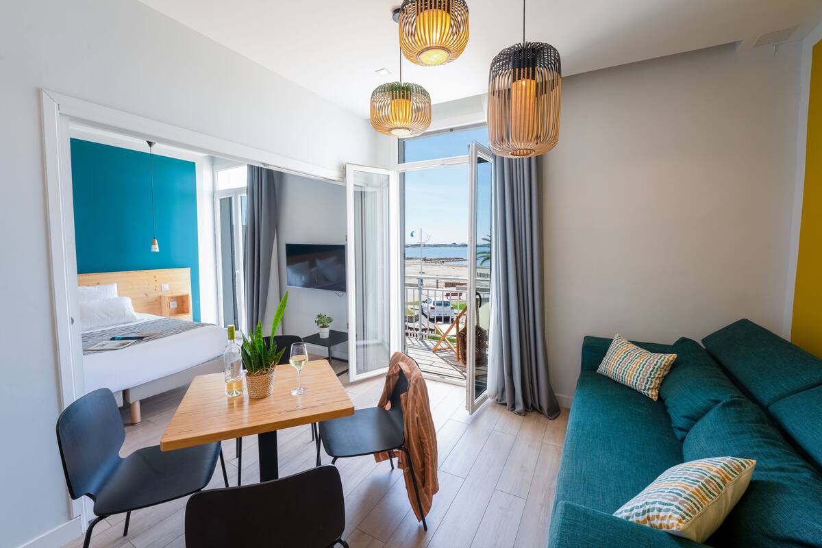 A modern hotel room with a balcony, a dining area, and a sofa.