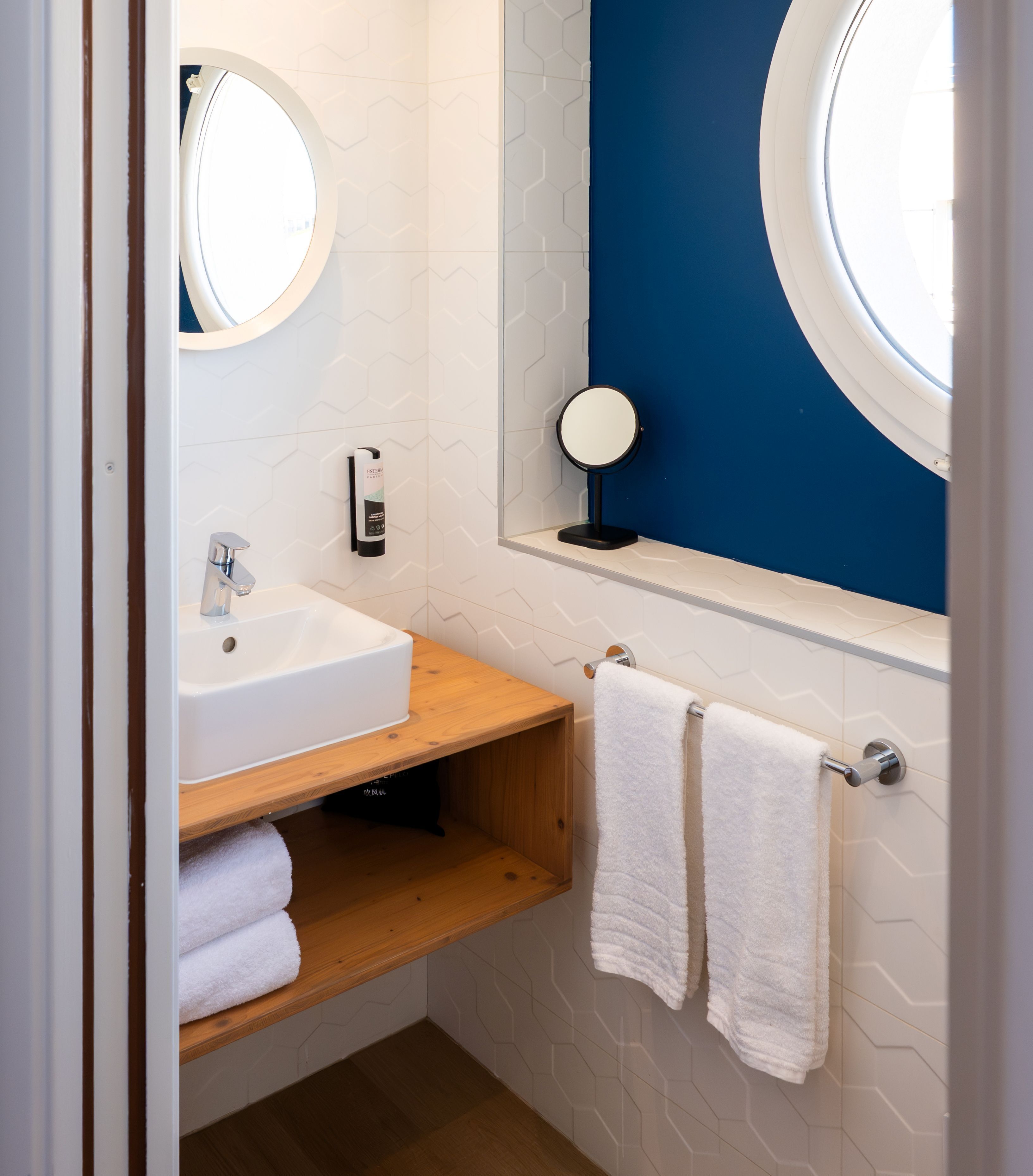 Een badkamer met een witte wasbak, een houten plank, twee handdoeken, een spiegel en een blauwe accentmuur.