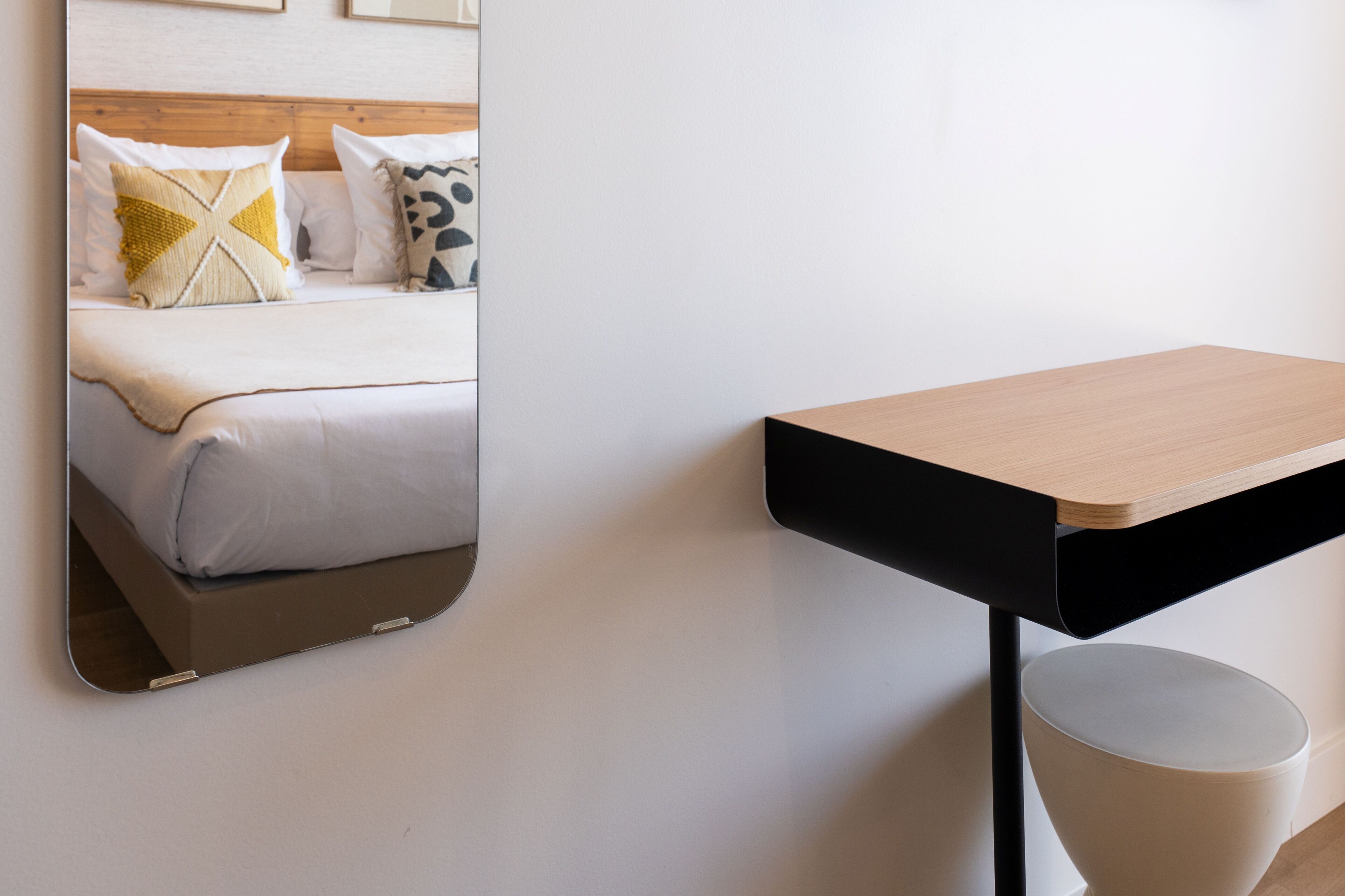 A modern hotel room with a bed, a side table, and a mirror reflecting the bed.
