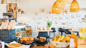 A café with wicker baskets of bread and fruit, a coffee machine, and hanging wicker lamps. - Hôtel Café Miramar (Le Grau-Du-Roi)