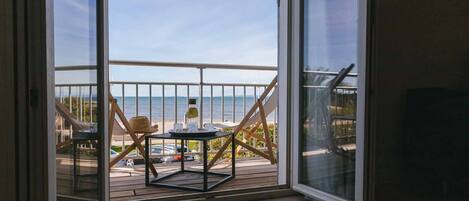 Un balcon doté d’une terrasse en bois, une table avec deux chaises et une vue sur la plage et l’océan.