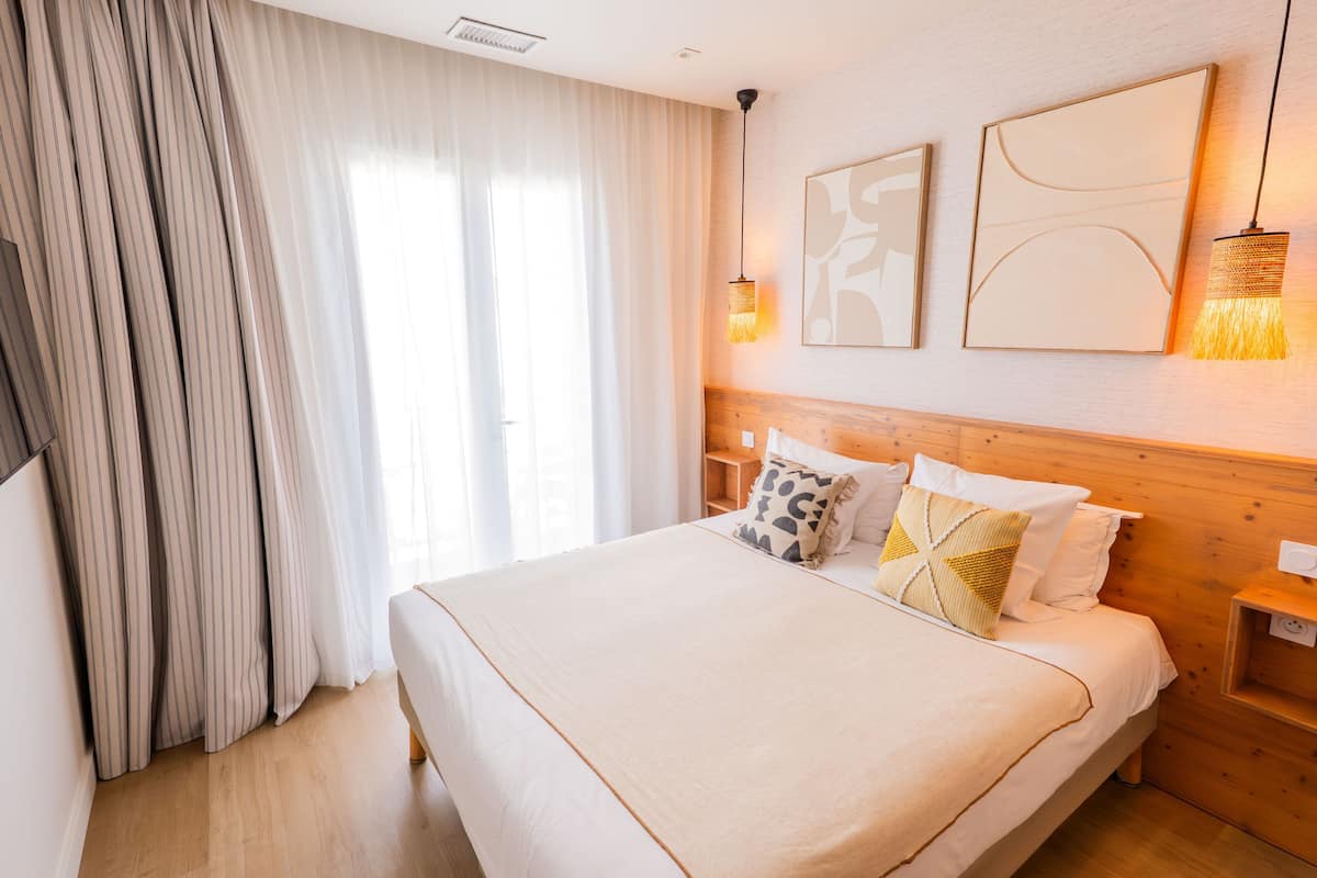 A hotel room with a large bed, curtains, wall art, and a nightstand.