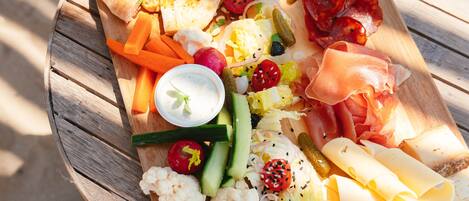A wooden board with various cheeses, meats, vegetables, and dips.