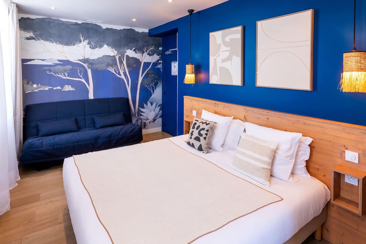 A bedroom with a bed, a sofa, a wall mural, and two wall-mounted lights.