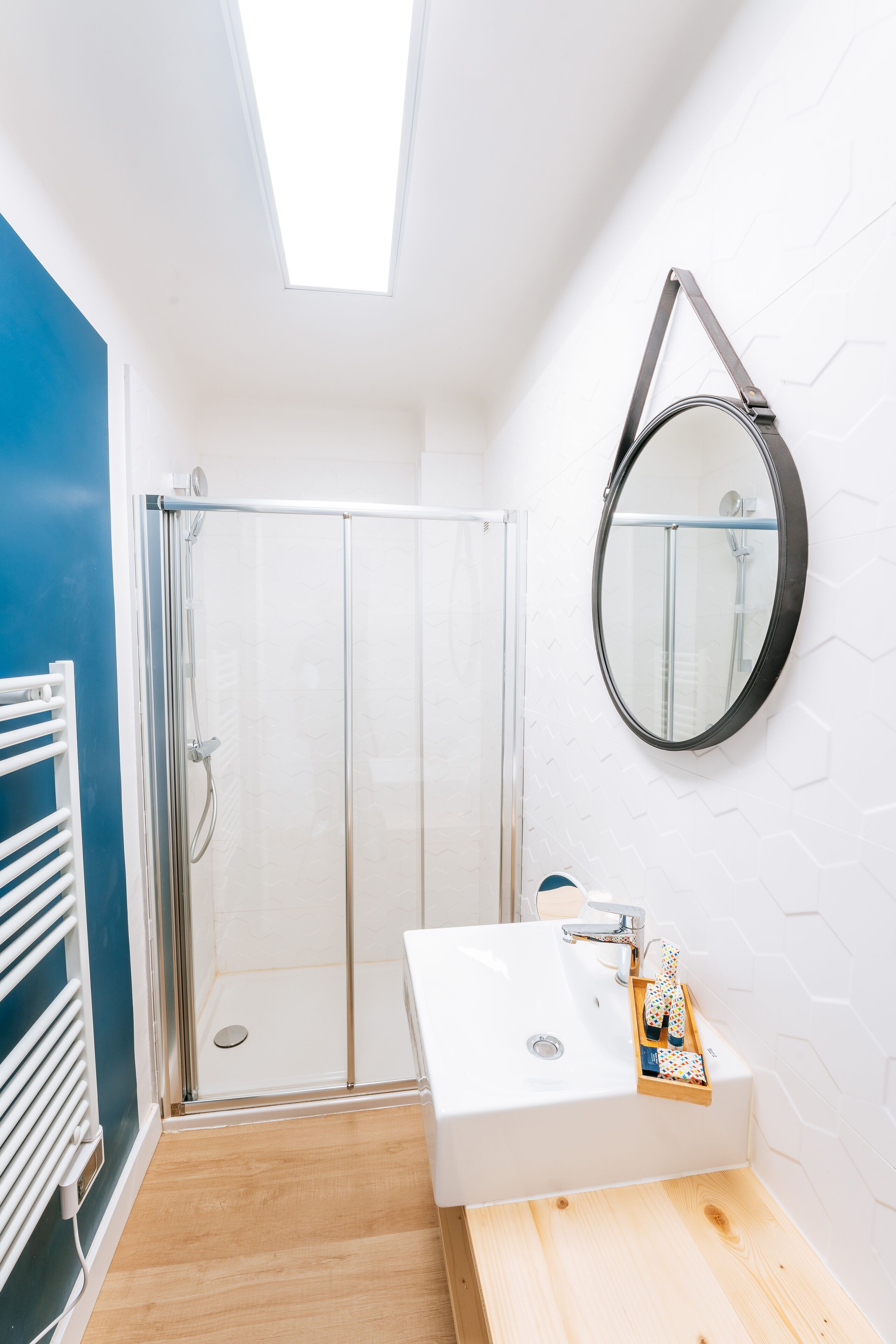 A bathroom with a glass shower enclosure, a white sink with a tray, and a round mirror.