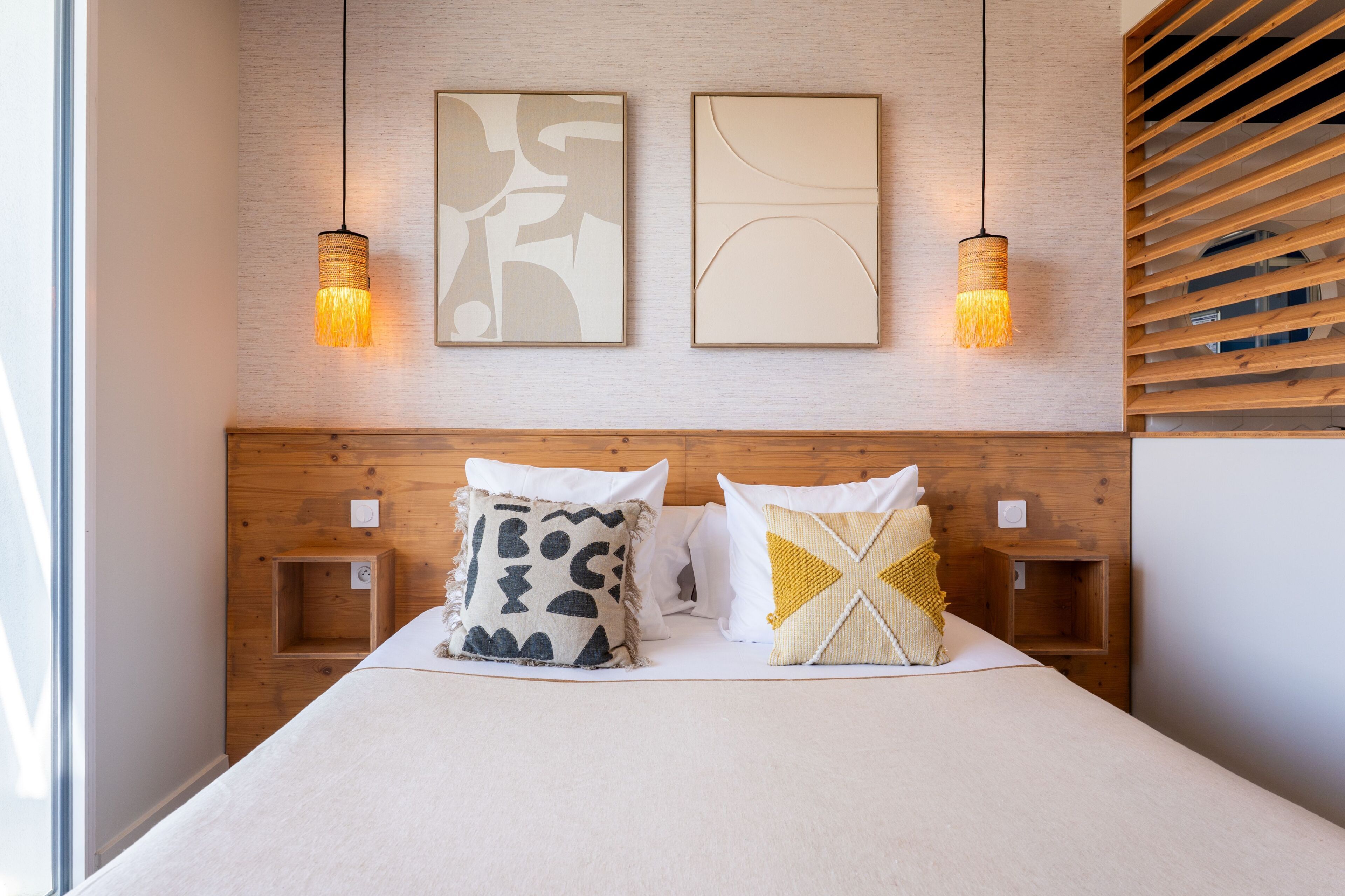 Una cama bien ordenada con dos almohadas, un cabecero y dos lámparas fijadas a la pared.