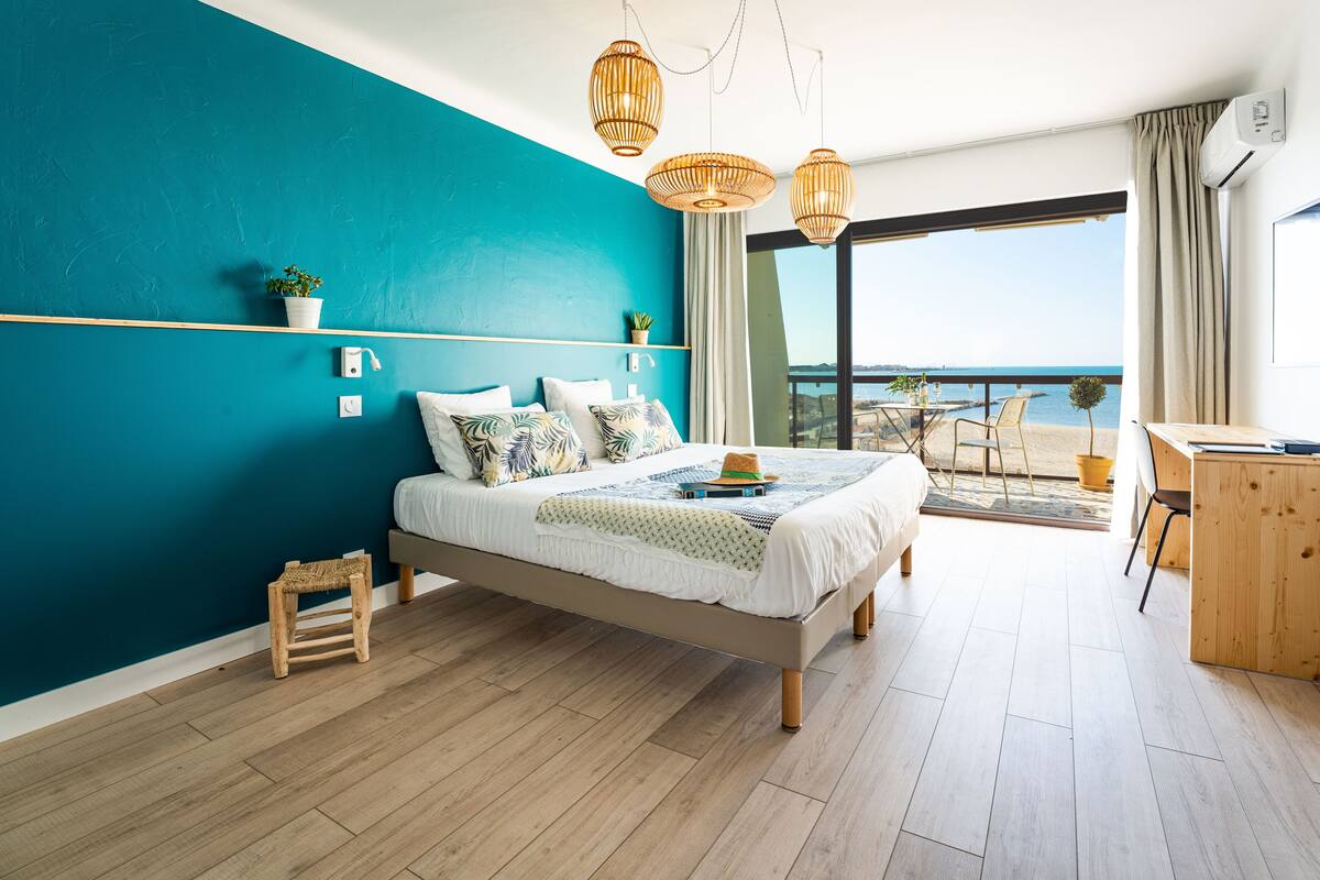 A bedroom with a bed, bedside tables, a desk, and a balcony with a view.