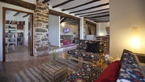 Una sala de estar acogedora con un pilar de piedra, vigas de madera, un sofá y un televisor.