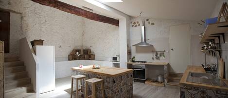 A spacious kitchen with a large island, wooden stools, a built-in oven, and a high chimney.