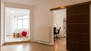 A spacious room with a wooden floor, a radiator, a desk with a chair, and a large sliding door. - Spacious Ultracentral Apartment Old City (Bucharest)