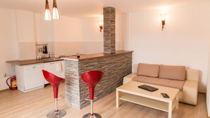 A modern kitchen with a stone island, a dining area with a sofa and a coffee table, and two red bar stools. - Spacious Ultracentral Apartment Old City (Bucharest)