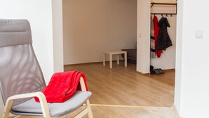 A room with a wooden bench, a chair with a red jacket, a small table, and a coat rack with jackets. - Spacious Ultracentral Apartment Old City (Bucharest)