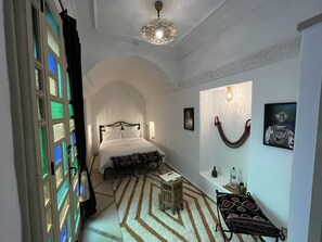 A bedroom with a bed, a nightstand, a wall-mounted lamp, and a decorative wall hanging. - Riad ECILA (Marrakech)