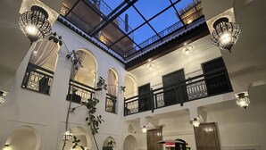 A spacious courtyard with a high ceiling and a skylight, featuring traditional arches, a fountain, and multiple seating areas. - Riad Ecila (Marrakech)
