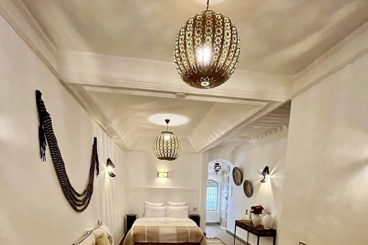 A hotel room with a bed, a sofa, a small table, and a hanging light fixture.