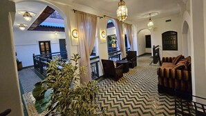 A spacious lobby with a patterned floor, a seating area with a sofa and chairs, and a staircase leading to an upper level. - Riad Ecila (Marrakech)