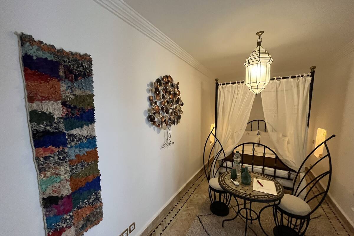 A room with a bed, a table with chairs, a wall-mounted lamp, and a colorful rug.