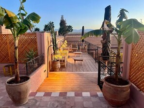 A rooftop terrace with potted plants, a seating area, and a view of the mountains. - Riad ECILA (Marrakech)
