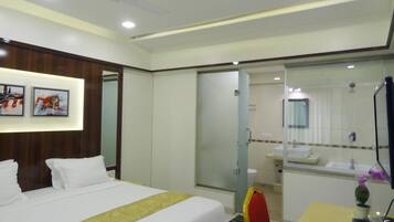 Habitación de hotel con cama, escritorio, silla, baño con ducha y espejo.