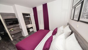 Une chambre d’hôtel moderne, dotée d’un grand lit, d’une télévision, d’une armoire et d’une salle de bain visible à travers une porte ouverte.
