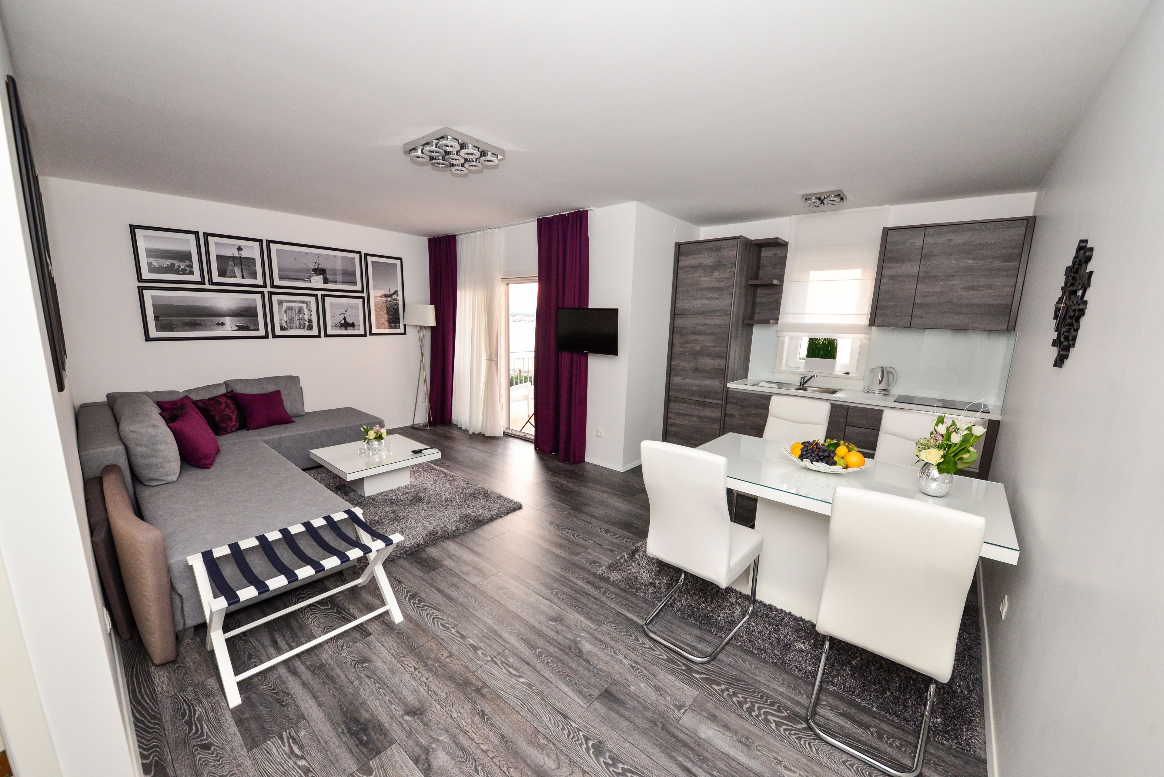 Un apartamento moderno con un sofá gris, una mesa de comedor con sillas, una zona de cocina y una sala de estar con televisor.