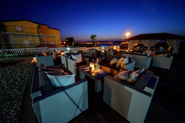 An outdoor seating area with wicker furniture and a view of the sea at dusk. - Sunset Apartments (Vir)