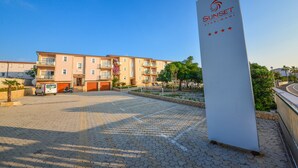 Un immeuble d’appartements moderne, avec un ciel dégagé, une cour pavée et une enseigne indiquant « Sunset Apartments ».