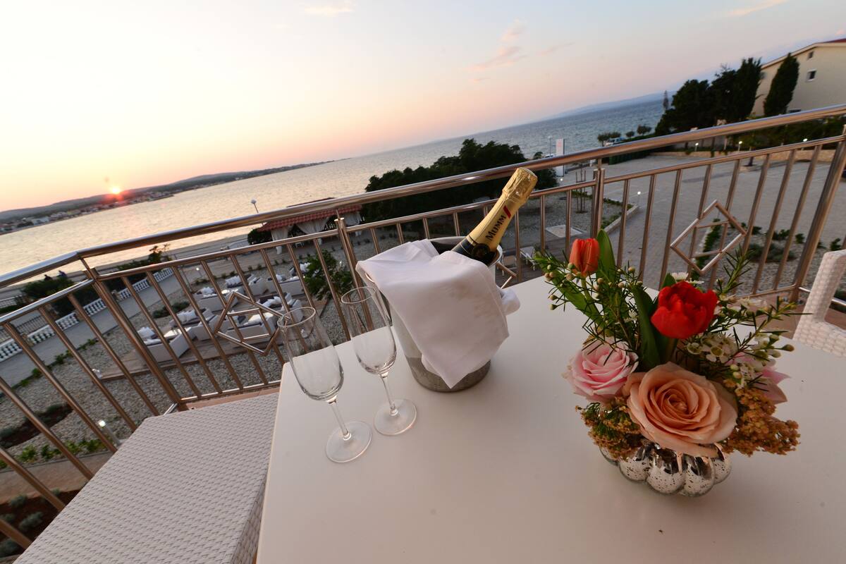 A balcony with a table set for two, a bottle of champagne, and a vase of flowers.