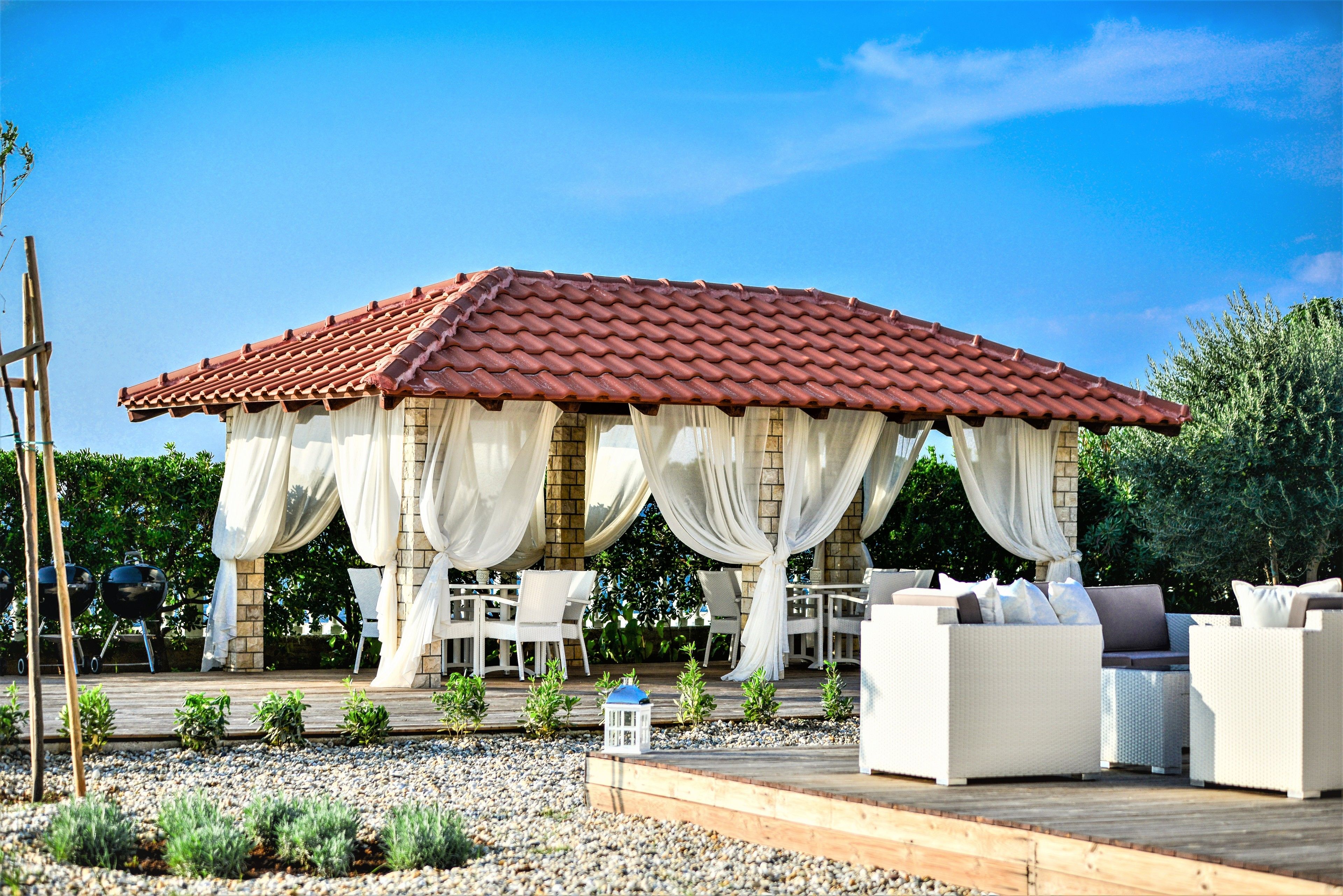 A covered outdoor seating area with white furniture and a red-tiled roof.
